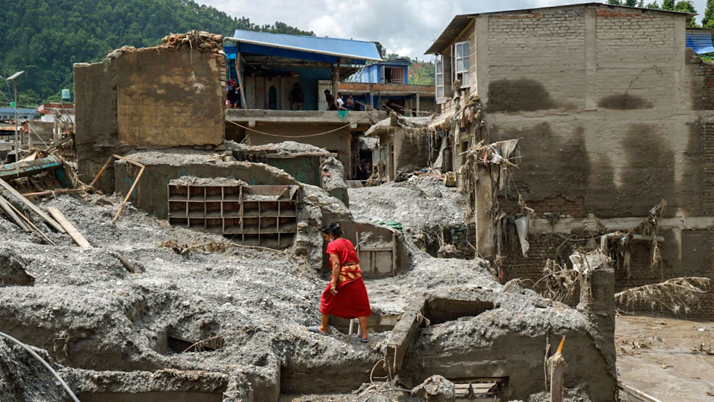 A woman climbs over the rubble of a destroyed house.