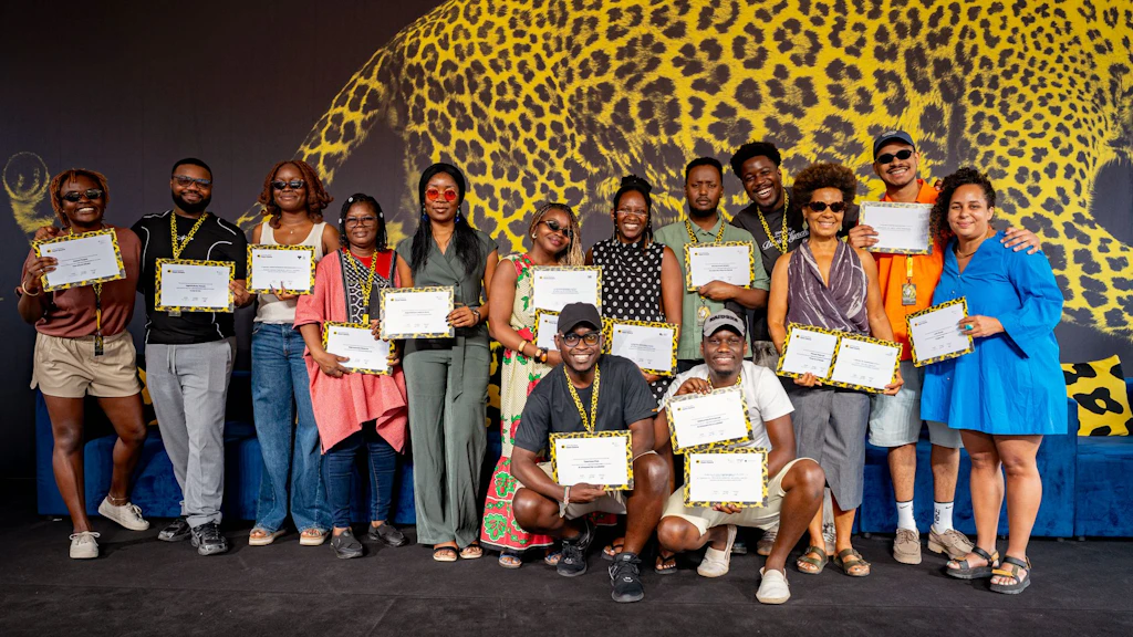 A group of smiling people are gathered on a stage and  are holding up the prizes they have won. 