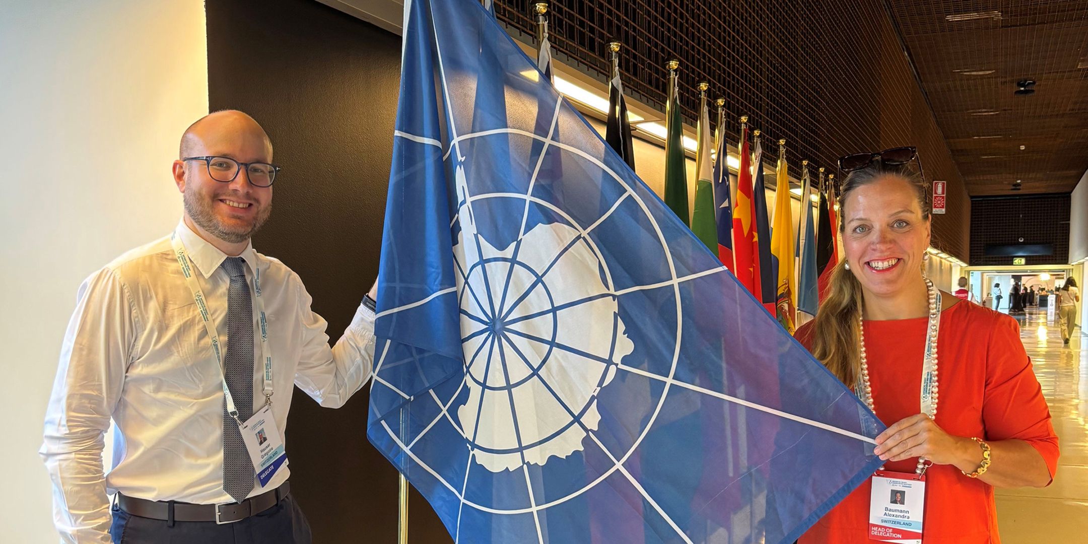 Grégoire Hauser and Ambassador Alexandra Baumann, with a flag depicting the polar region between them. 