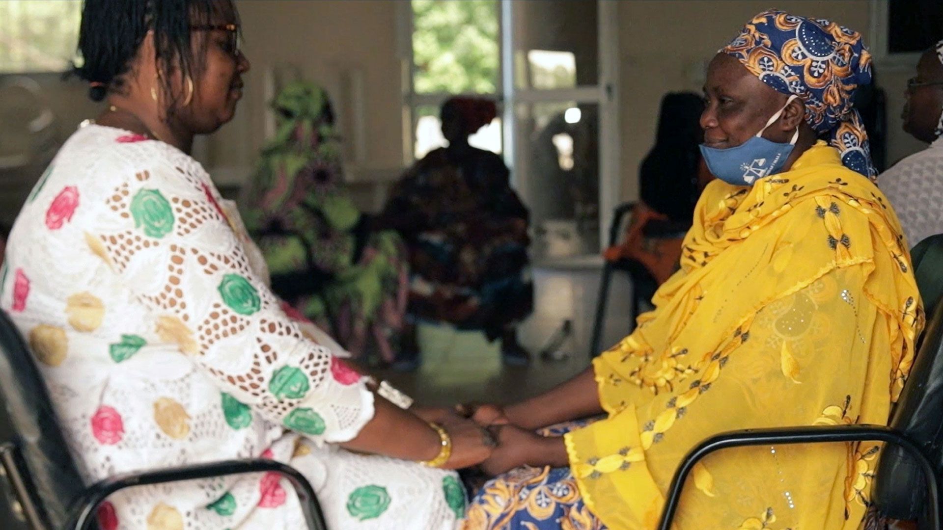Two women are sitting across from each other, looking at each other and holding hands
