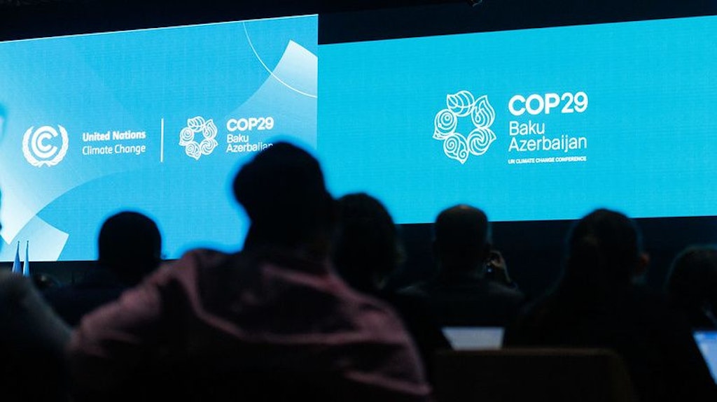 People in a large hall are looking at a blue glowing screen.