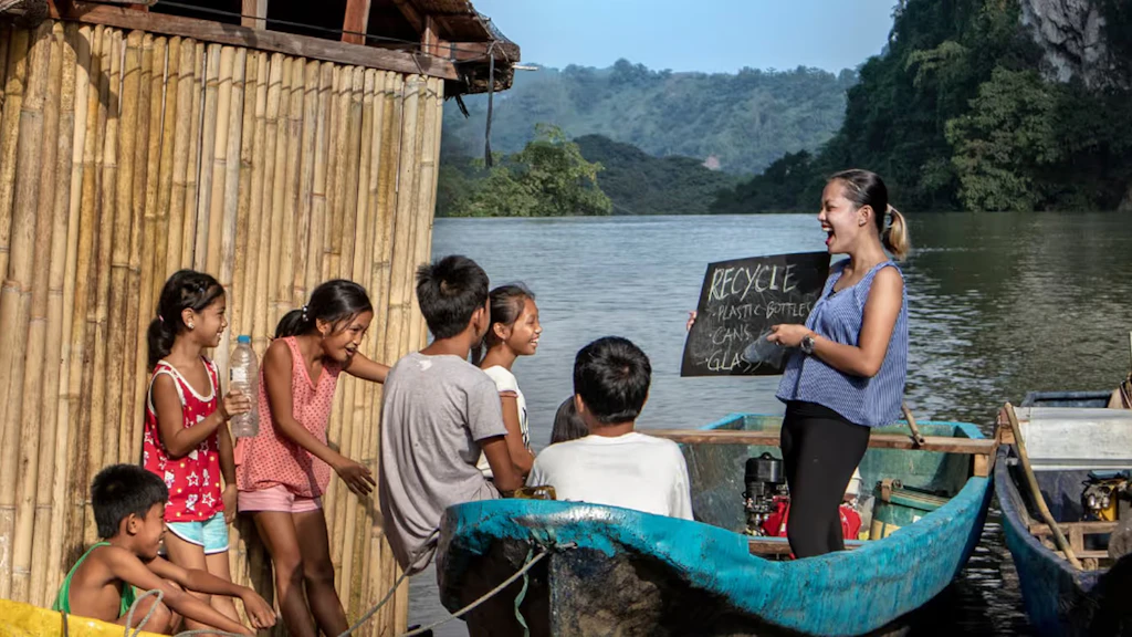 A young woman teaches children from a boat on a river in the Philippines.