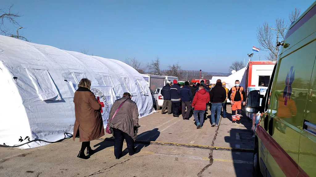 A white tent, an ambulance and other vehicles belonging to the civil protection authorities and humanitarian organisations. People working to provide assistance.
