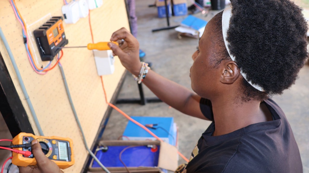 A young woman holding a screwdriver works on an electrical panel.
