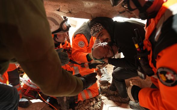 A man, surrounded by members of Swiss Rescue, cradling a four-month-old girl who has just been rescued from a fallen building.