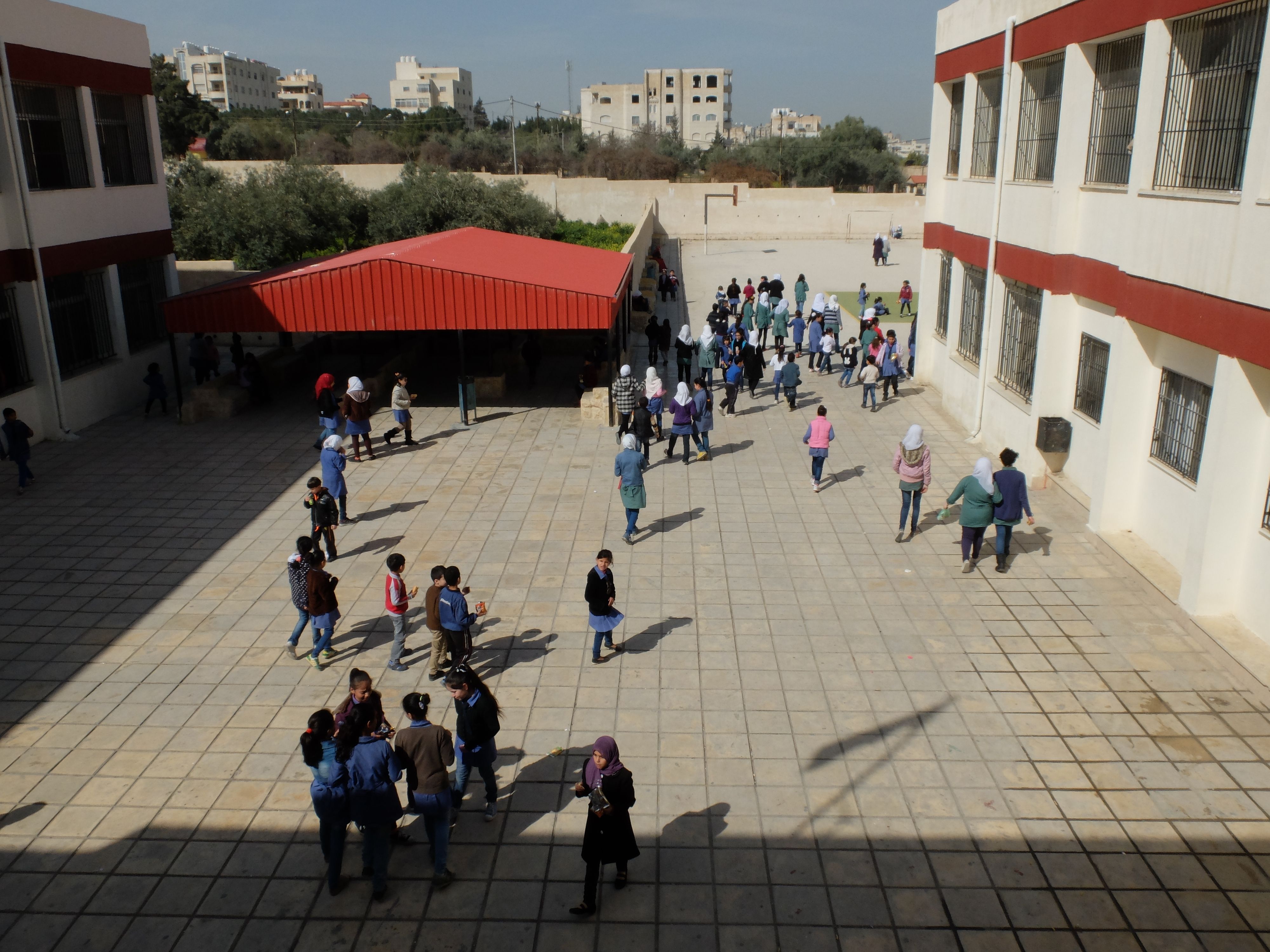 Girls and boys chat in groups or walk together towards the exit of the school building. Some of the girls are wearing white or coloured veils.