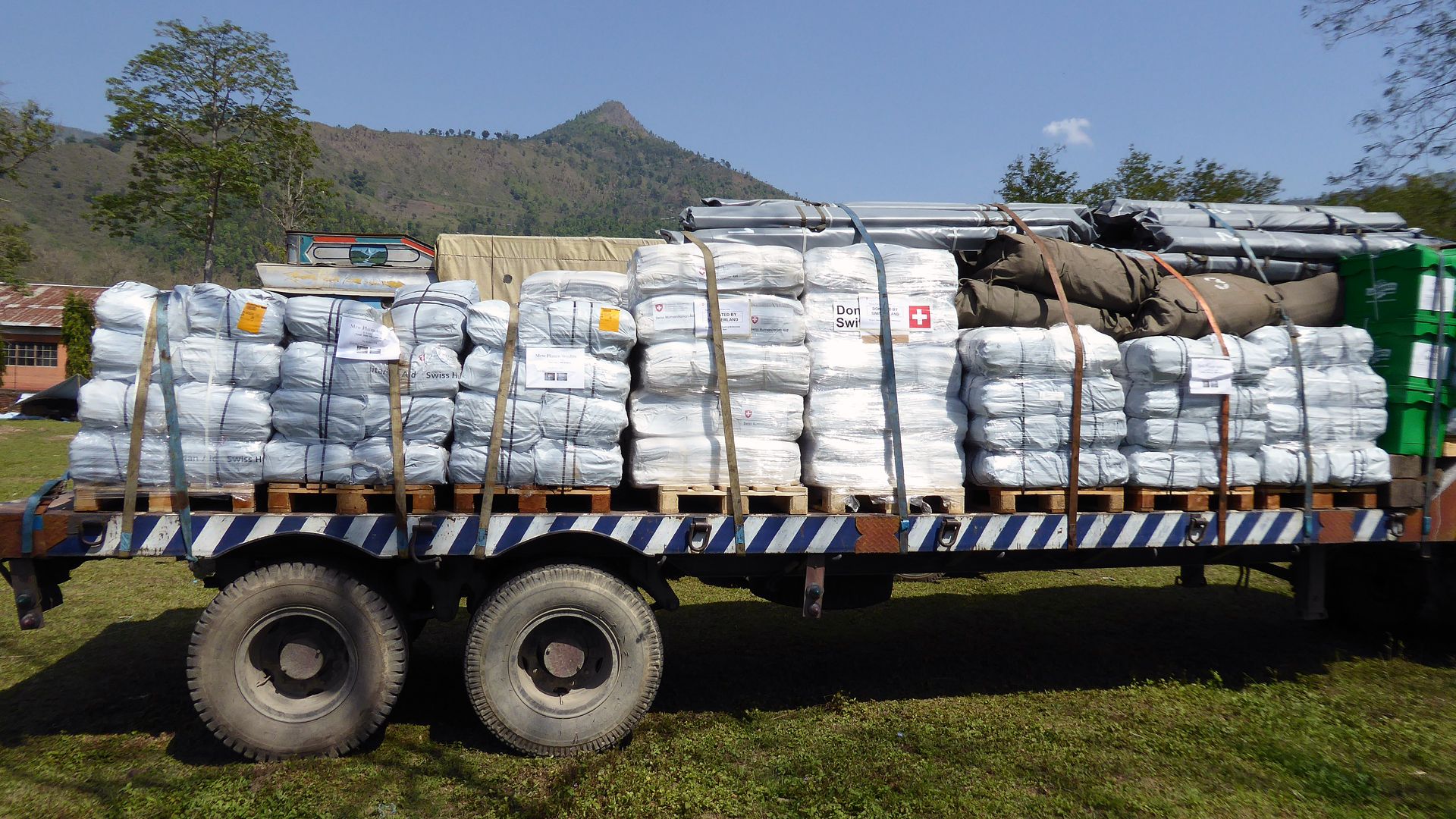 This photograph shows a truck loaded with relief supplies from Switzerland. Many white packages, building materials and long poles can be seen.