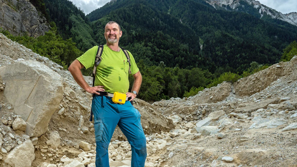 Eric Bardou se tient sur un éboulis, avec les montagnes en arrière-plan.