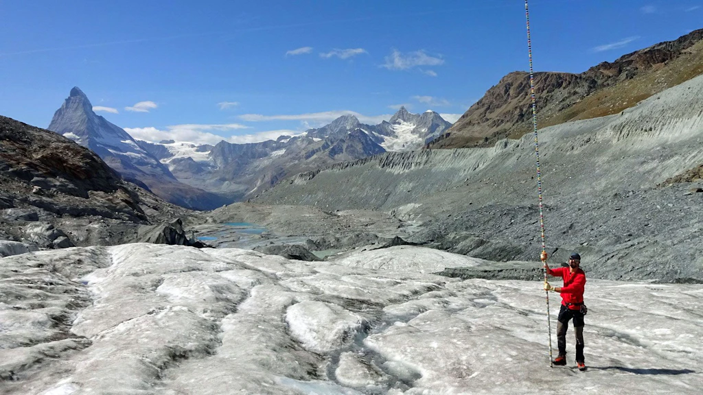 Un homme équipé d’une perche de mesure sur un glacier dans les Alpes suisses.