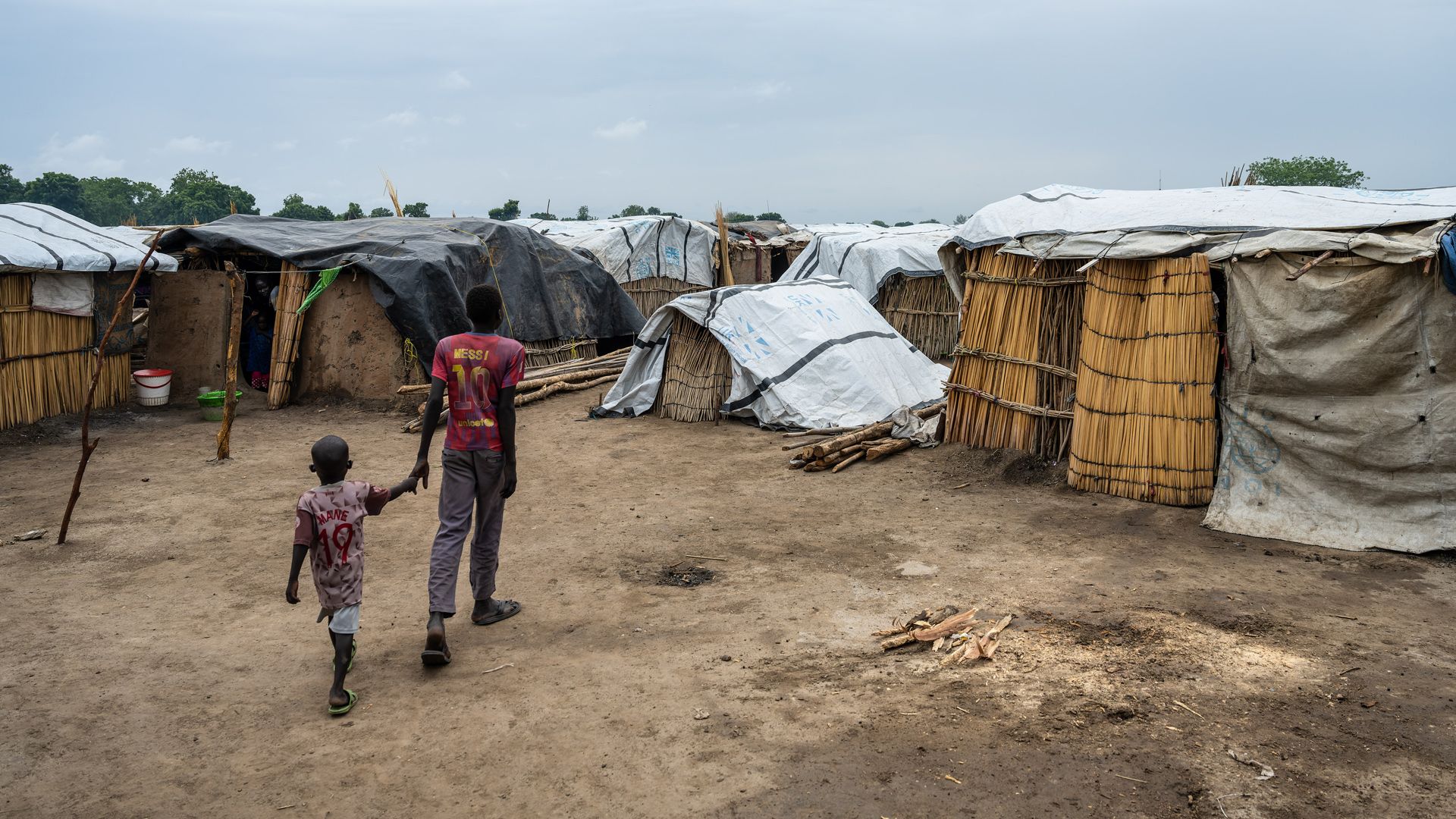 Deux enfants vus de dos se tiennent par la main dans un camp.