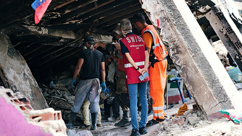Une experte et un expert suisses inspectent les dégâts près d’un bâtiment détruit.