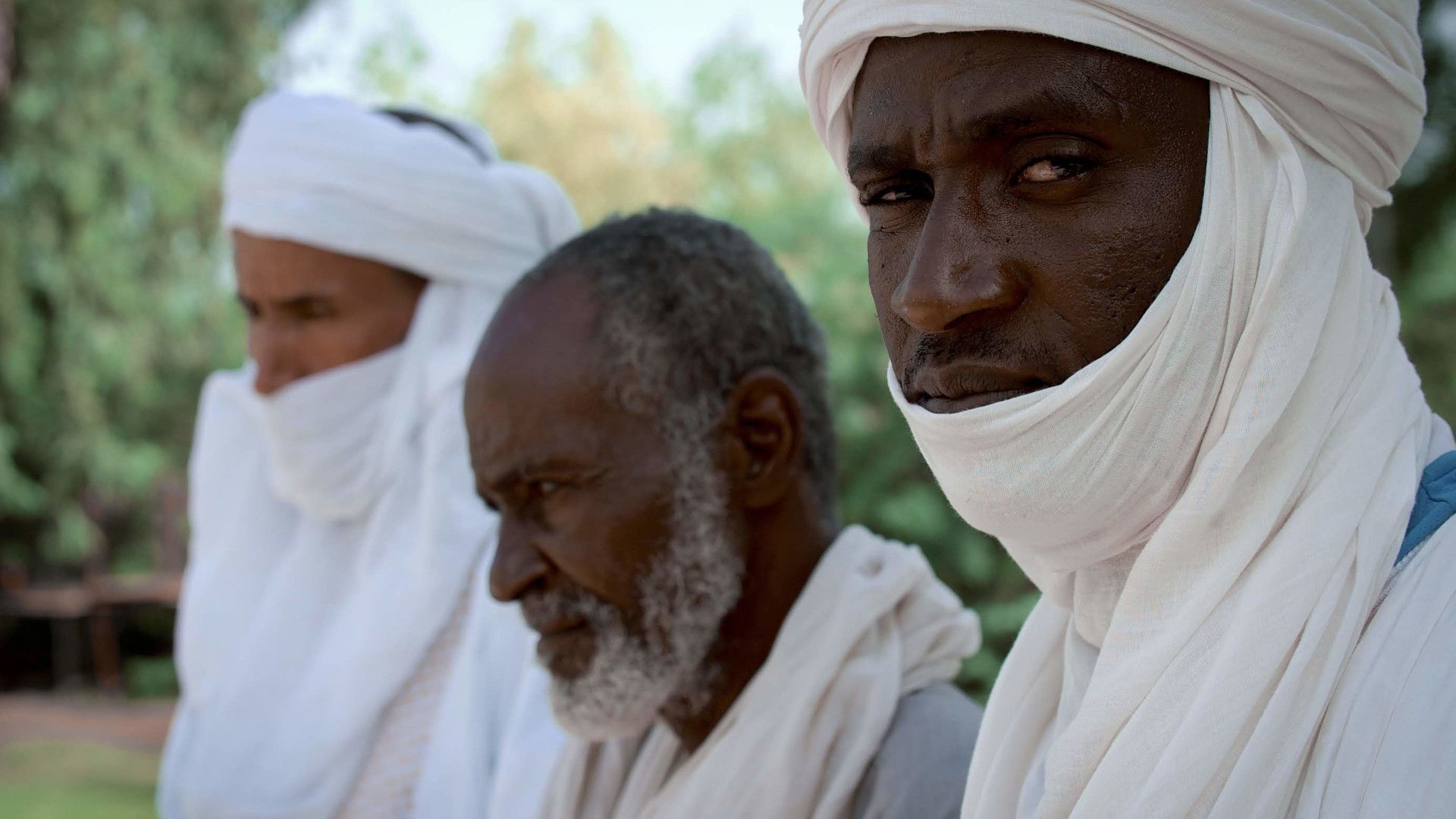 Trois hommes, dont deux portant des turbans blancs, se tiennent côte à côte, de profil.