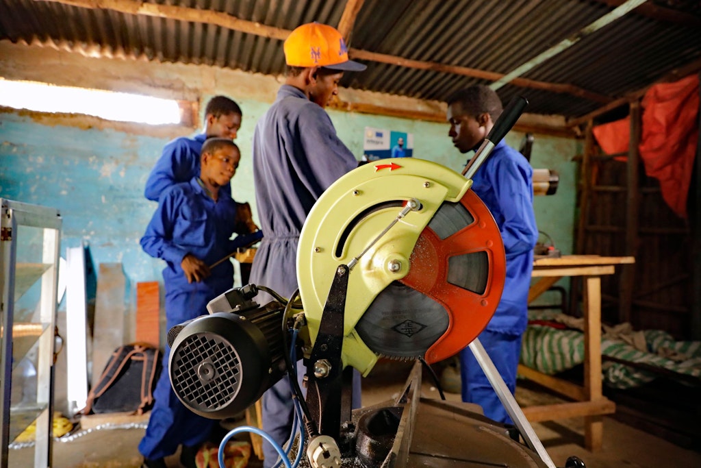Mamadou explique l’utilisation d’une machine à trois jeunes apprentis vitriers en combinaison bleu foncé.