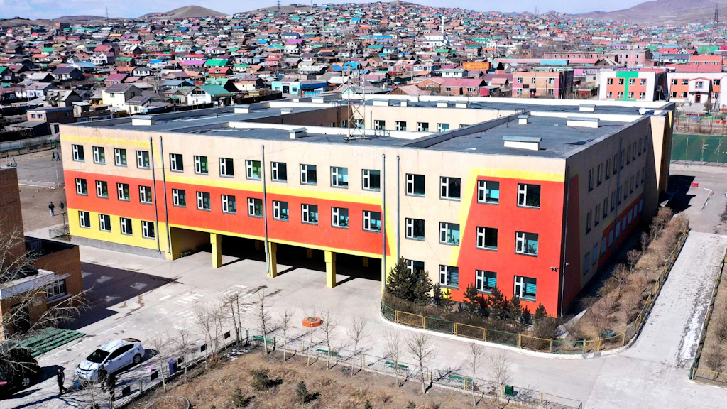 Vue aérienne d'un bâtiment scolaire rénové en Mongolie, avec une façade rouge et jaune,entouré d'un quartier de maisons.