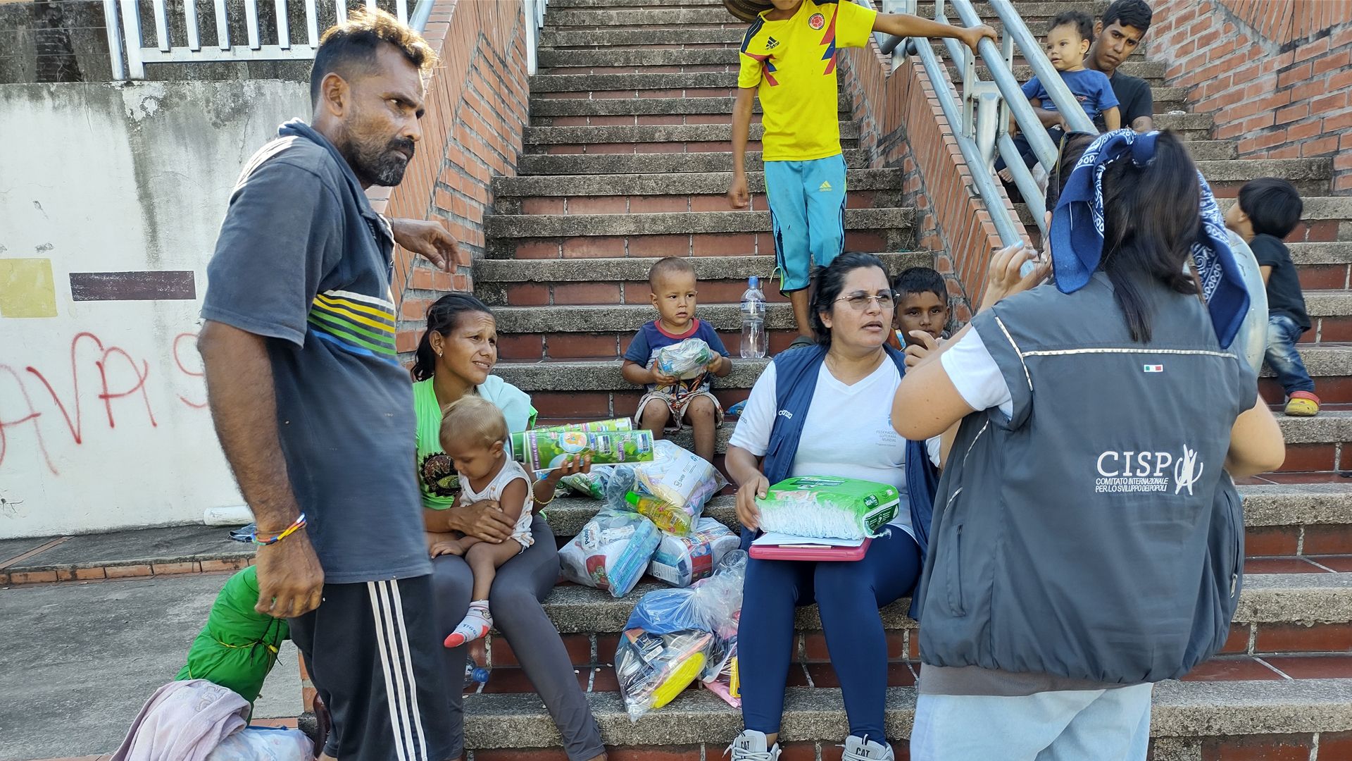 Des personnes portant un gilet muni du logo de l’ONG distribuent des produits d’hygiène, de l’eau et des compléments alimentaires aux personnes dans le besoin.
