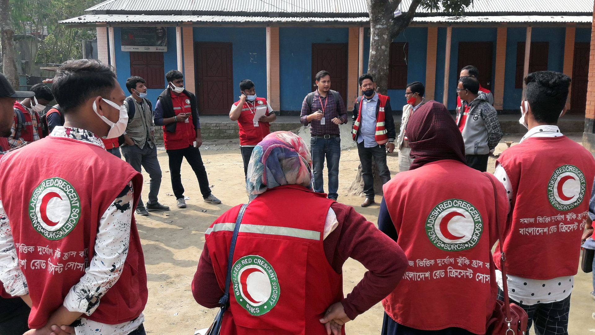 Réunis dans une cour extérieure, des volontaires du Croissant-Rouge discutent avec des représentants de communautés locales.
