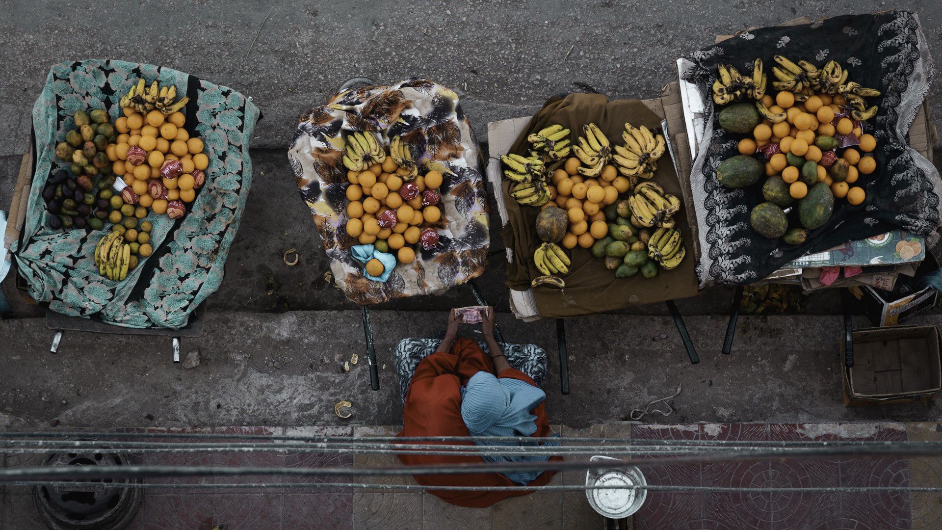 Vue aérienne d’une marchande de fruits au camp de réfugiés de Kakuma, au Kenya, assise devant un étal coloré.