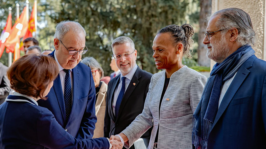 La présidente Gordana Siljanovska-Davkova accueille le président de la Confédération Guy Parmelin d’une poignée de main ; à ses côtés, la directrice de la DDC Patricia Danzi et d’autres membres de la délégation suisse ; en arrière-plan, des drapeaux macédoniens.
