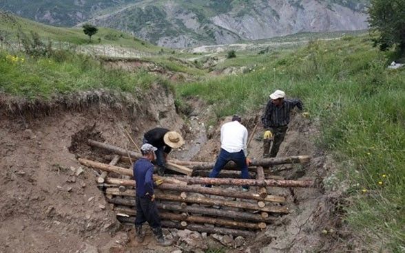  Quatre hommes construisent un barrage en bois simple mais résistant sur le flanc d'une montagne.
