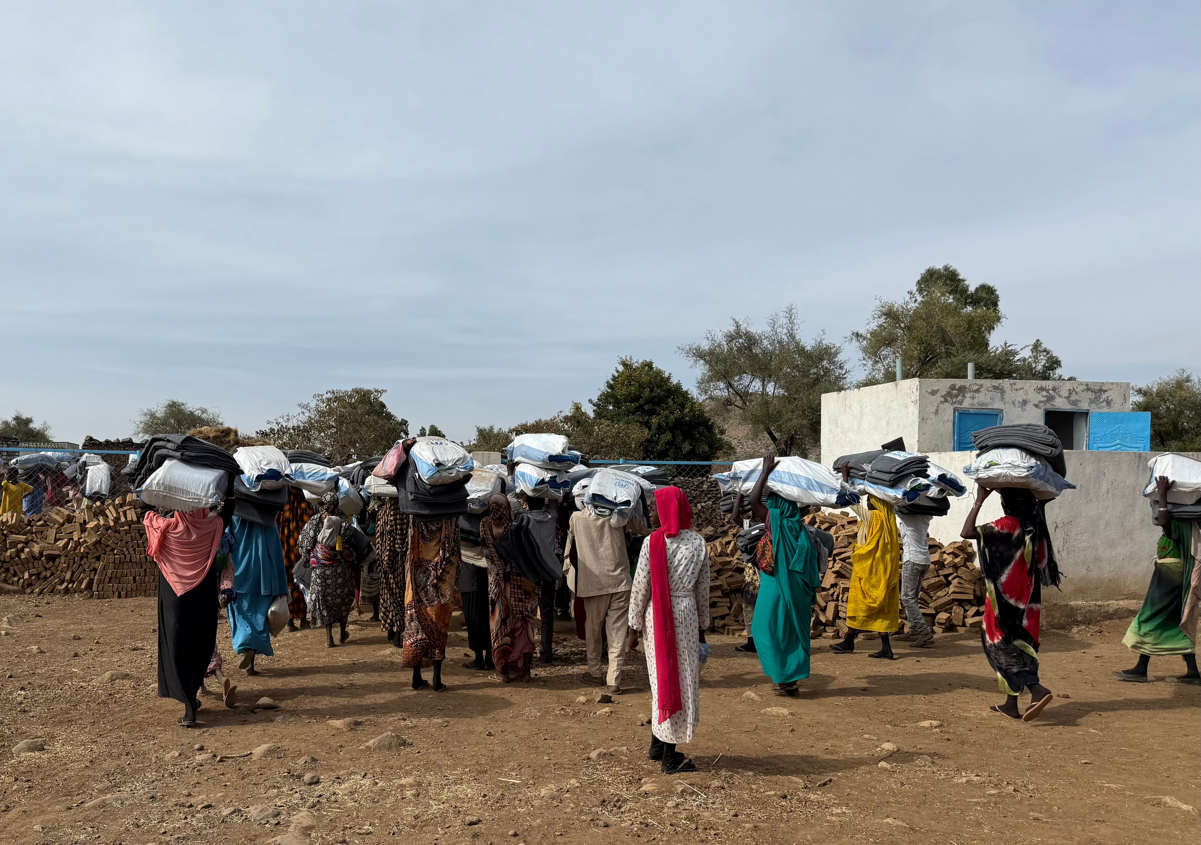 Des hommes et des femmes déplacés marchent de dos portant sur leur tête des sacs de première nécessité distribués par DRC