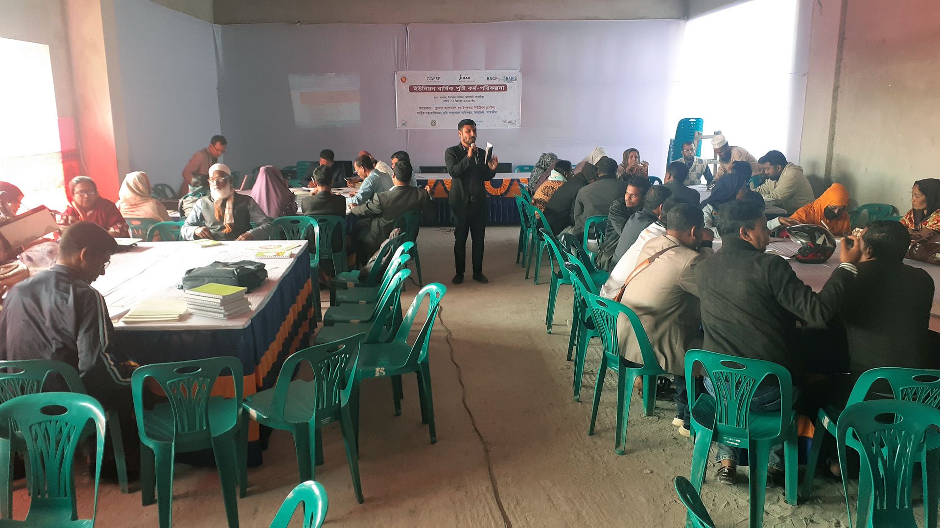 Dans une salle de réunion, assis autour de plusieurs tables, les membres du Budhata Union Council discutent.