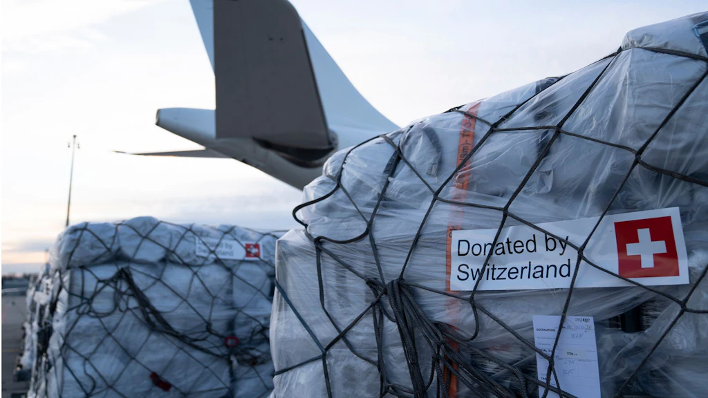 Une palette avec des cartons d’aide humanitaire devant un avion.