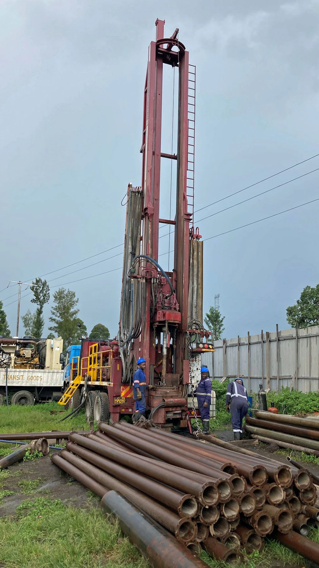 Des hommes portant des casques installent des équipements de forage pour un puits à Goma en RDC. Une pile de tubes est posée au sol.