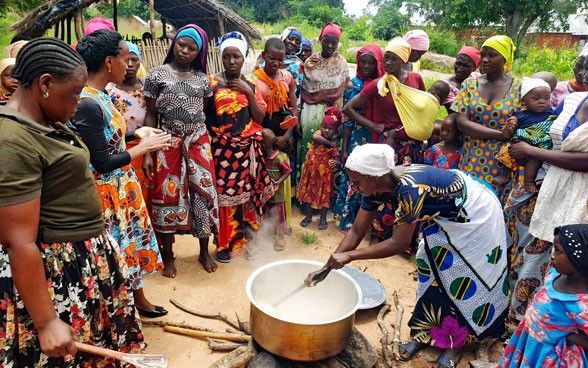 De nombreuses femmes entourent un chaudron sur le feu en Tanzanie. Au centre, une cuisinière remue l'eau et les grains à cuire.