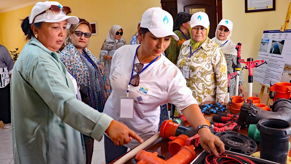 Des femmes portant une casquette à visière examinent des éléments de conduites en plastique et en métal, au milieu de câbles et d’autres matériaux de construction.
