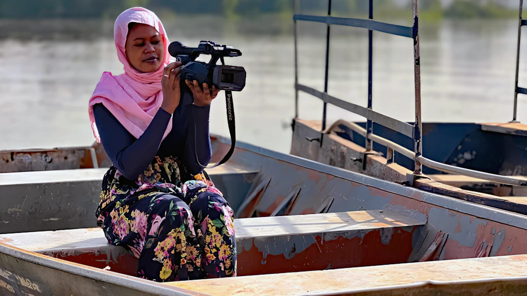 Une femme se trouve sur une barque avec une caméra lors d'un tournage de film.  