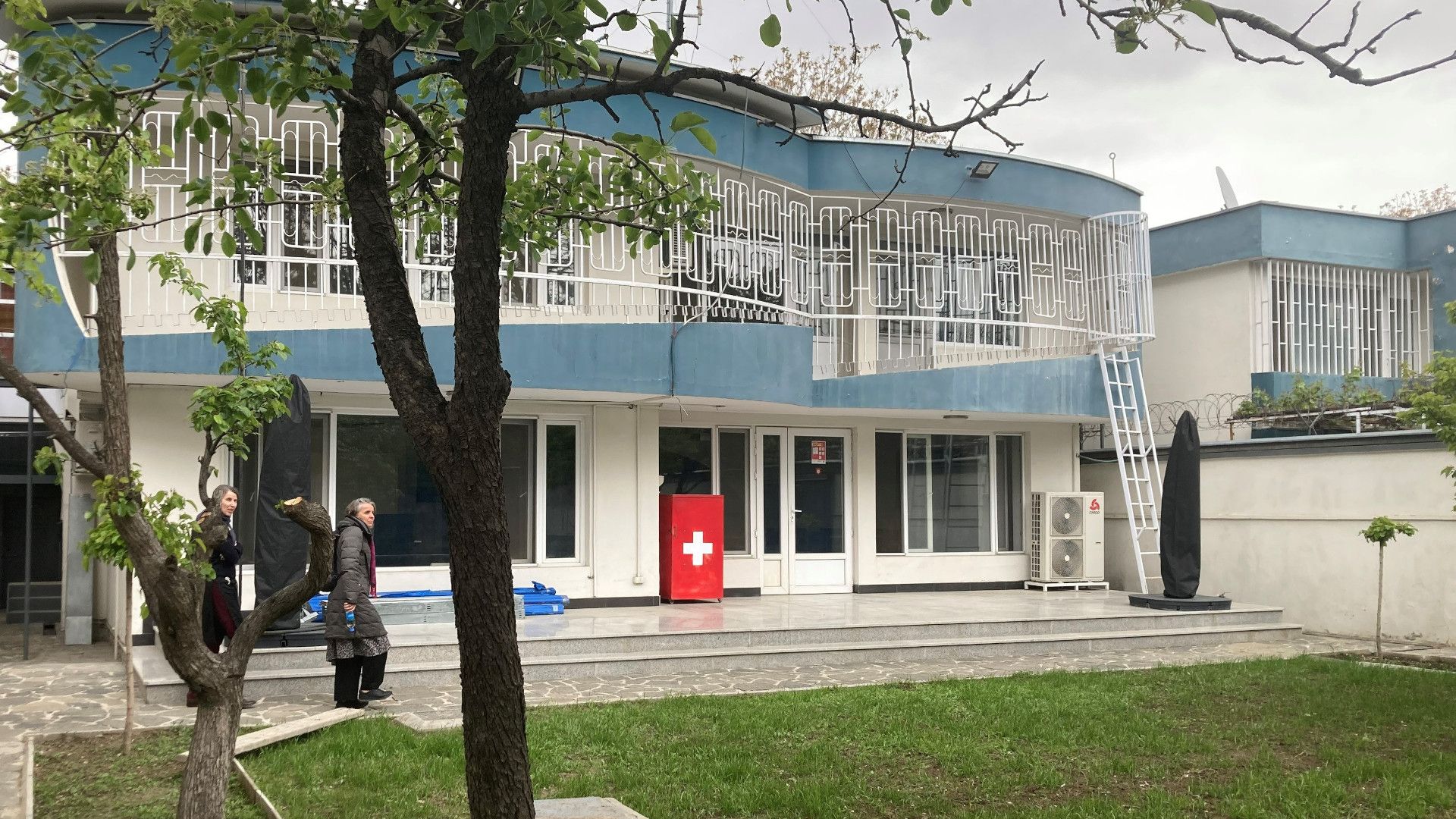 Vue du bâtiment du bureau humanitaire de la Suisse à Kaboul. Une pelouse et deux arbres sont visibles au premier plan.