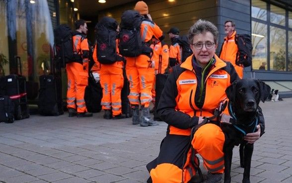 Une femme est agenouillée à côté de son chien et fait face à la caméra.