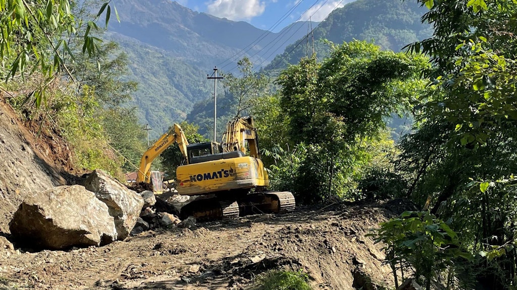 Une pelleteuse se trouve sur la route et enlève des pierres de la chaussée.