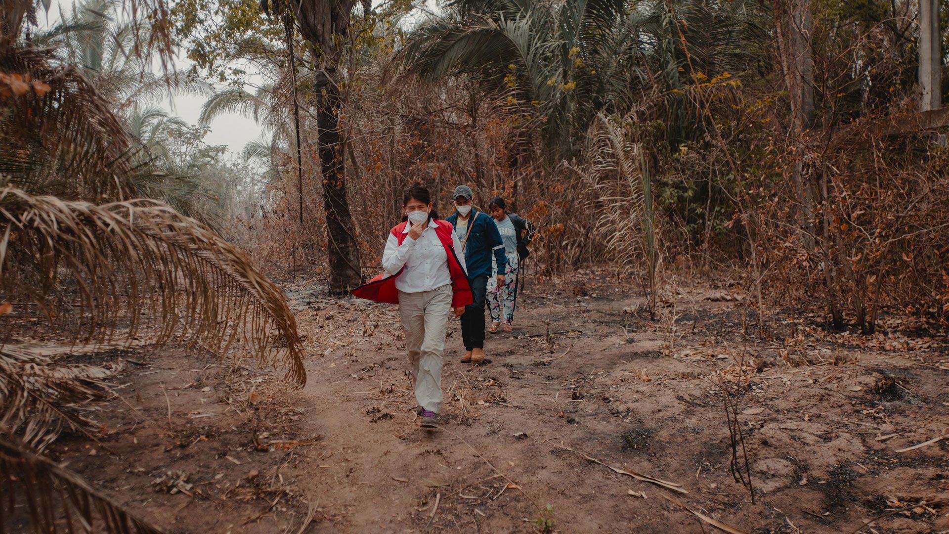 Un membro del team, accompagnato da un uomo e una donna, cammina nella foresta bruciata.