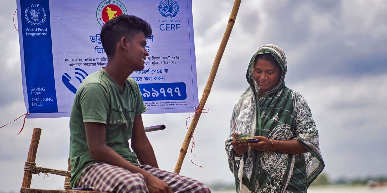 Sulla riva di un fiume in Bangladesh, una donna in compagnia del figlio conta il denaro ricevuto grazie a un programma di azione preventiva.