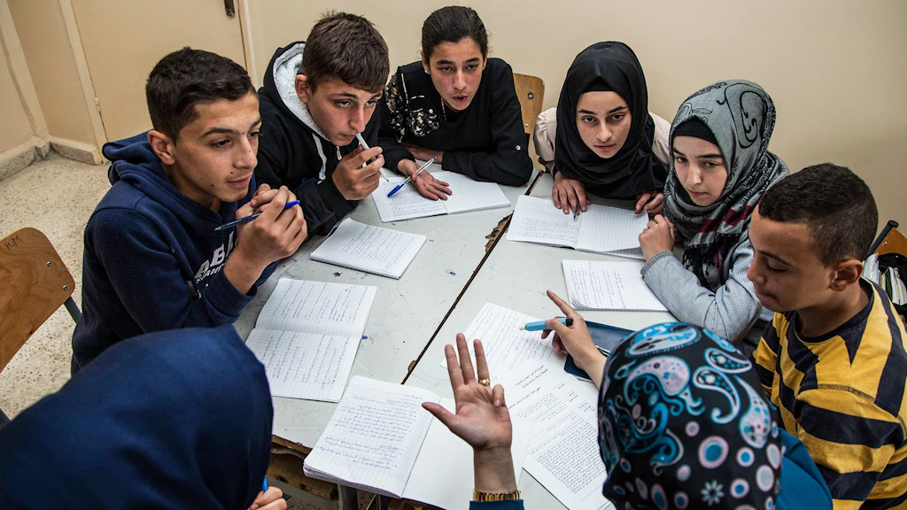 Un gruppo di giovani è seduto attorno a un tavolo. Insieme fanno risolvono dei compiti scolastici.
