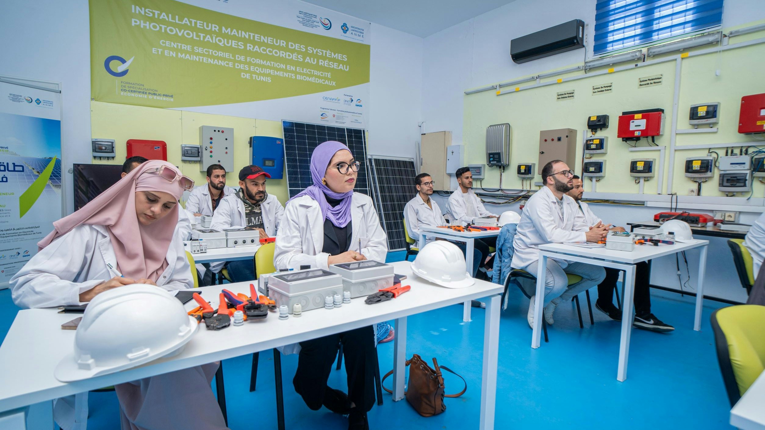 Un gruppo di uomini e donne seduti attorno a dei tavoli durante un corso di formazione sull'installazione di impianti fotovoltaici.