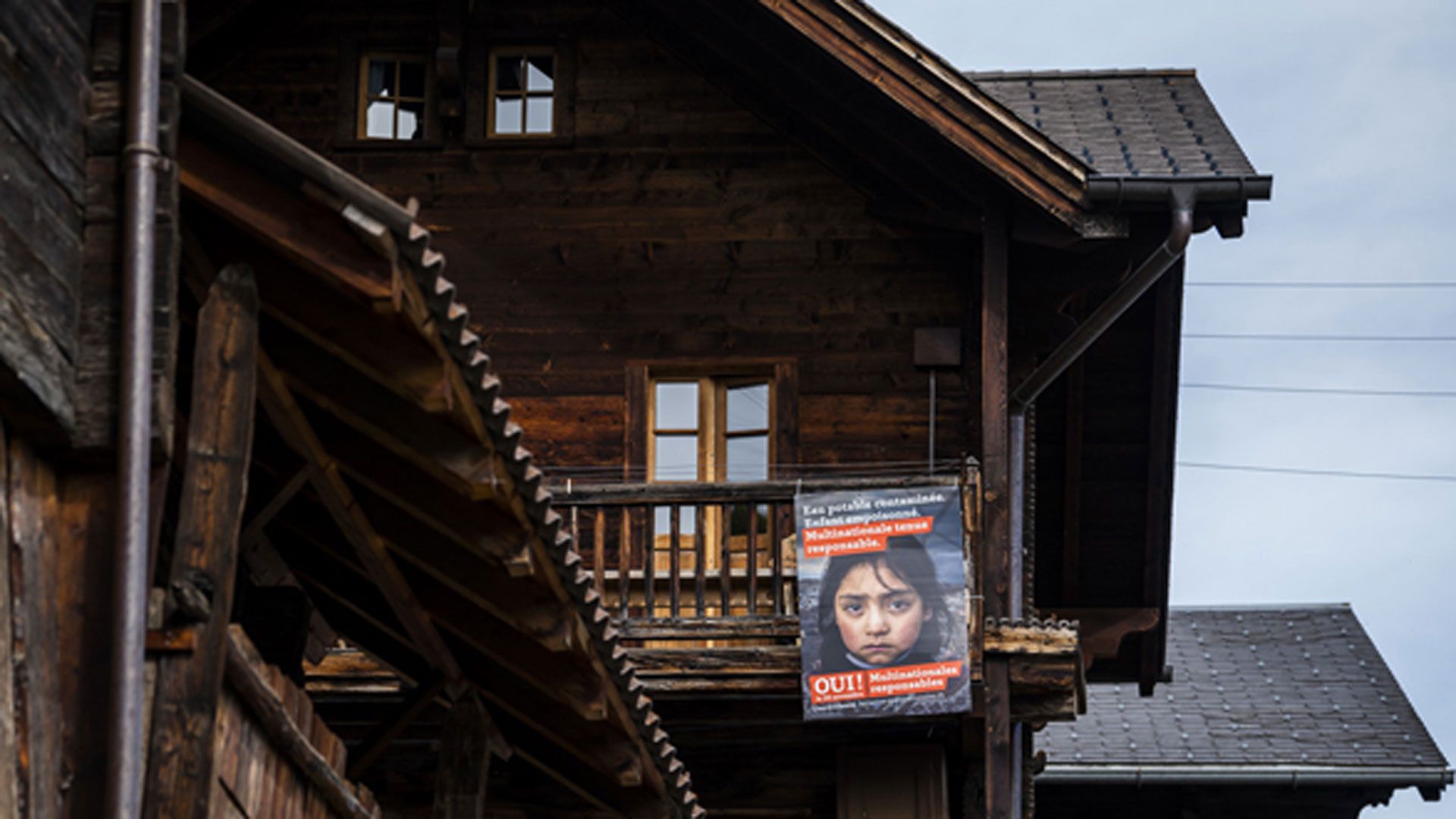 Un manifesto arancione per la votazione sull’«Iniziativa per multinazionali responsabili» su un vecchio fienile di montagna in legno scuro.