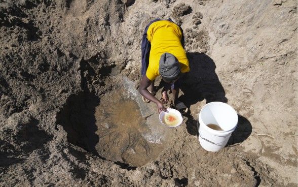 Una donna del posto attinge l’acqua da una buca nel terreno.