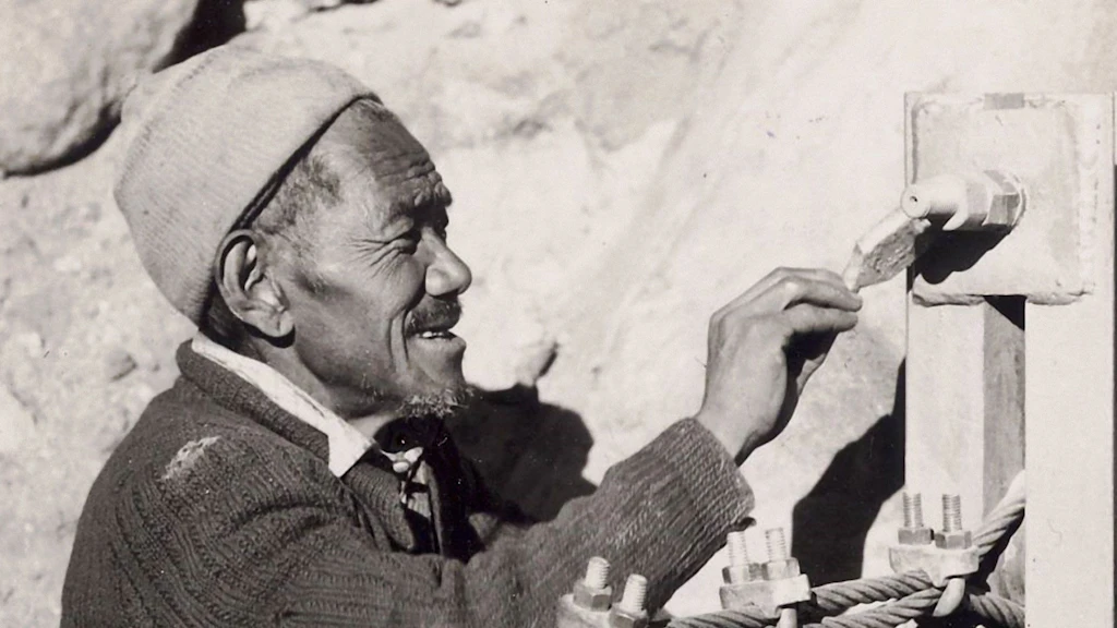 Il nepalese Ang Tsering Sherpa dipinge con vernice e pennello un elemento del ponte.