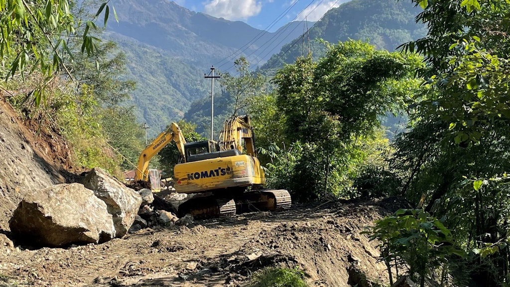 Un escavatore è fermo sulla strada e sta rimuovendo dei sassi dalla carreggiata.